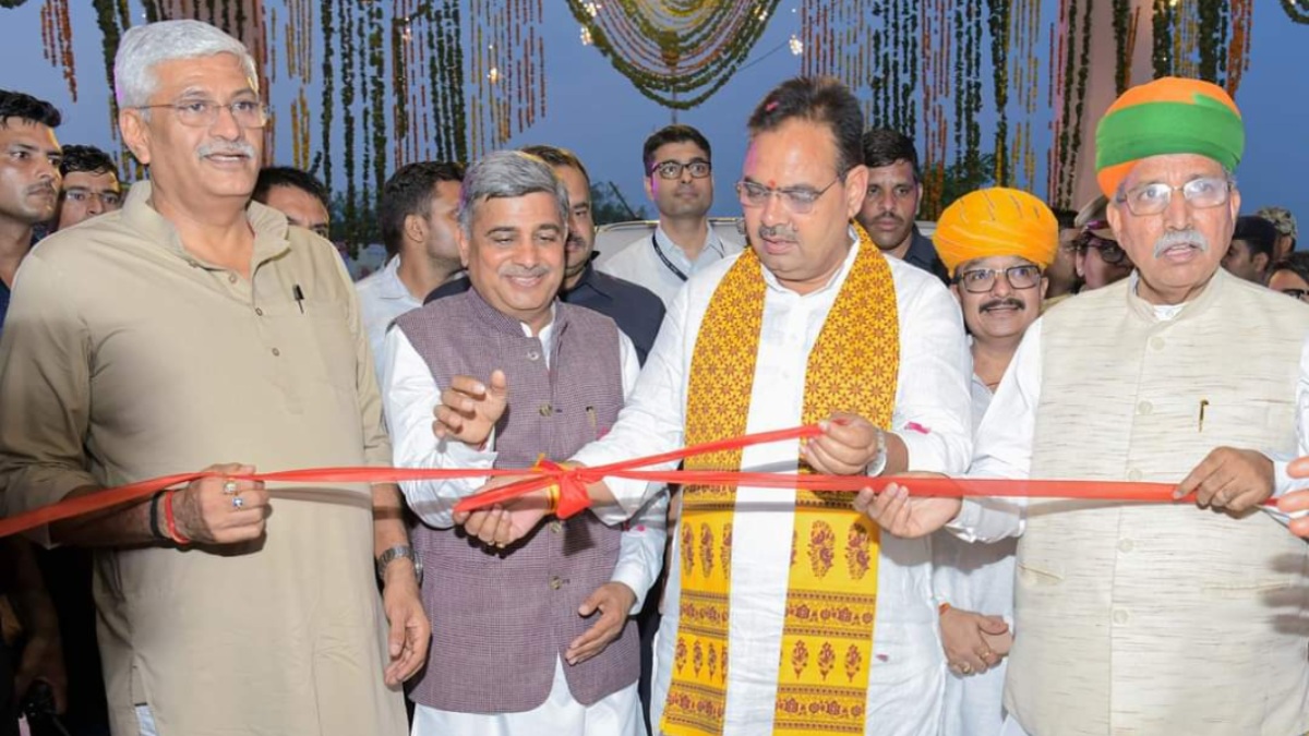 A red ribbon being cut at an outdoor inauguration beneath marigold garlands; Narsi Kularia in a purple waistcoat stands beside a man in white wearing a yellow printed stole, with other dignitaries on either side
