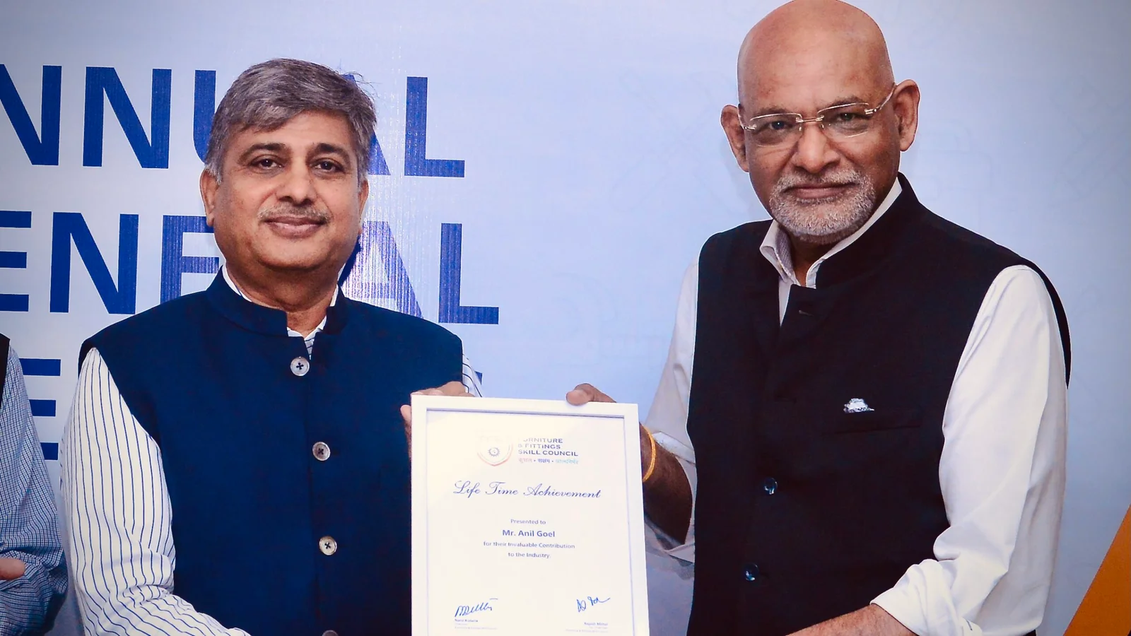 Narsi Kularia in a navy bandhgala jointly holding a framed Life Time Achievement certificate with a man in a black waistcoat